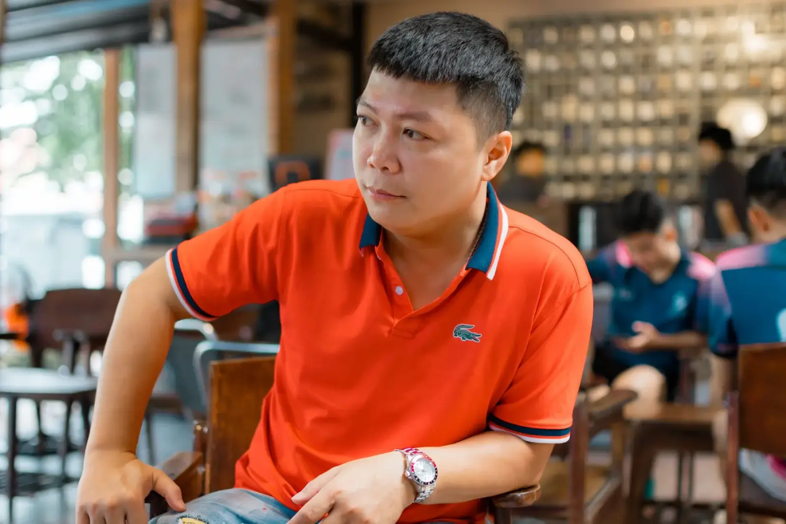 Người đàn ông mặc áo polo đỏ ngồi trong quán cà phê ấm cúng