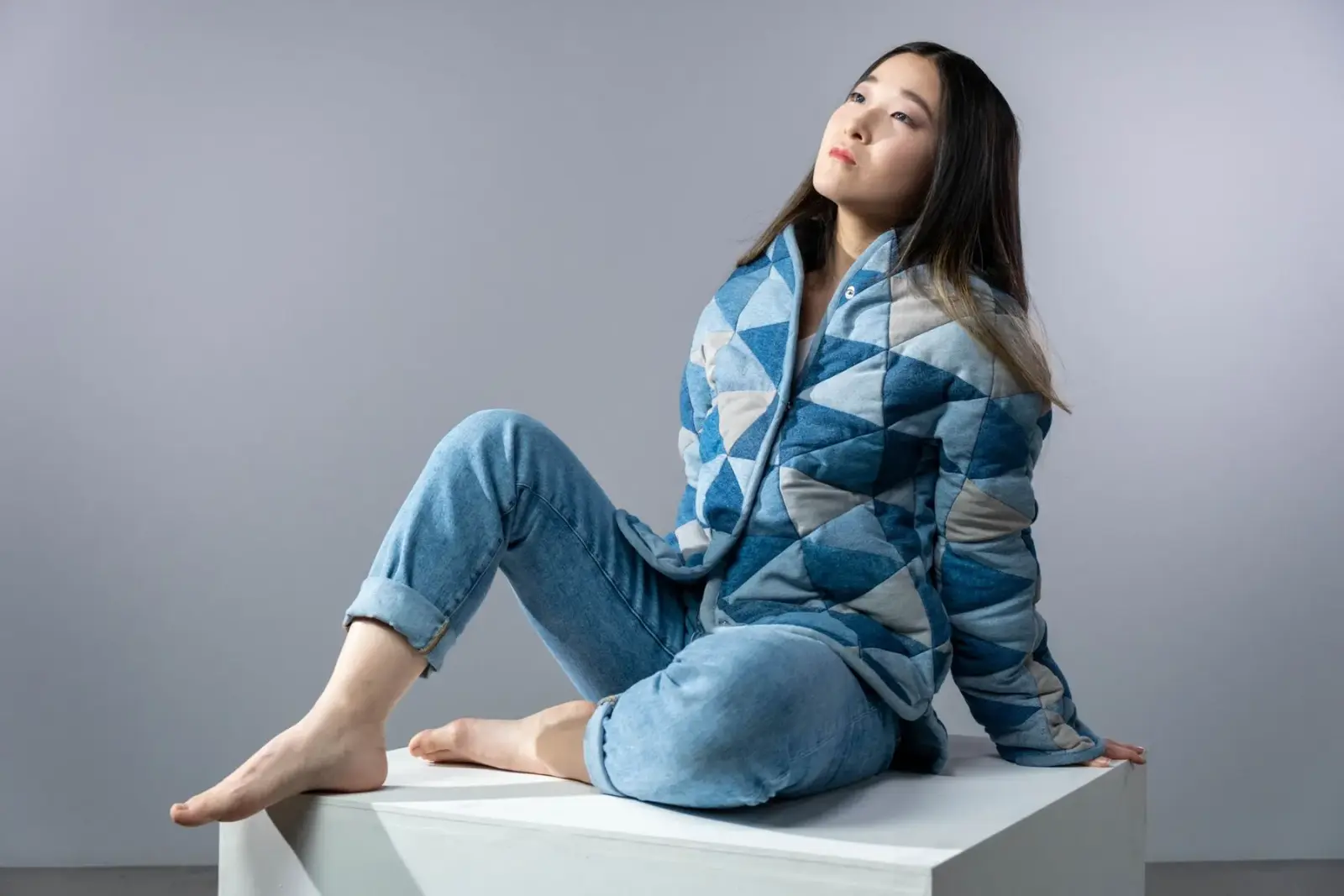 Người phụ nữ mặc quần jean và áo khoác hoạ tiết ngồi trên bục trắng