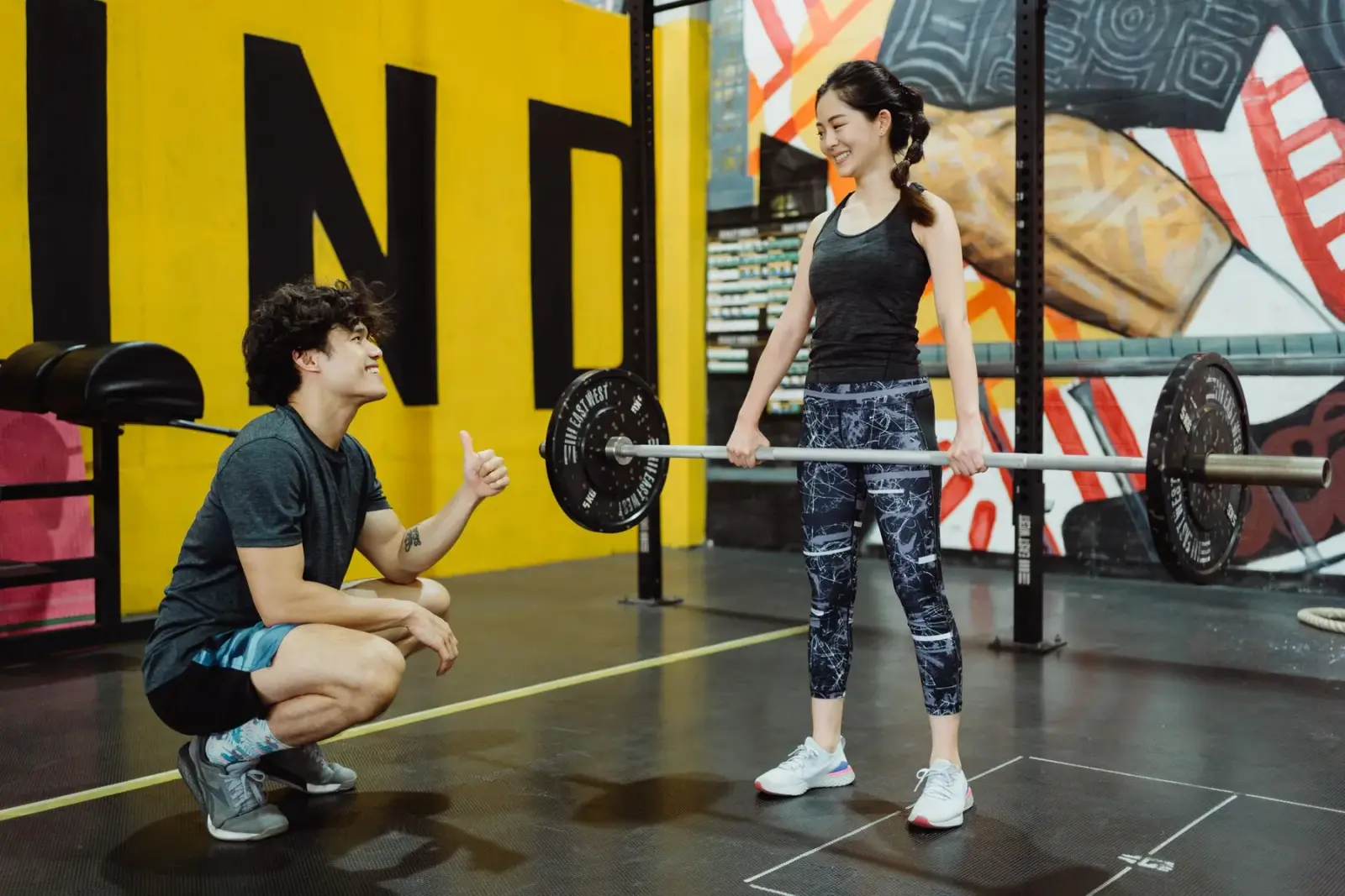 Người phụ nữ tập tạ trong phòng gym cùng huấn luyện viên