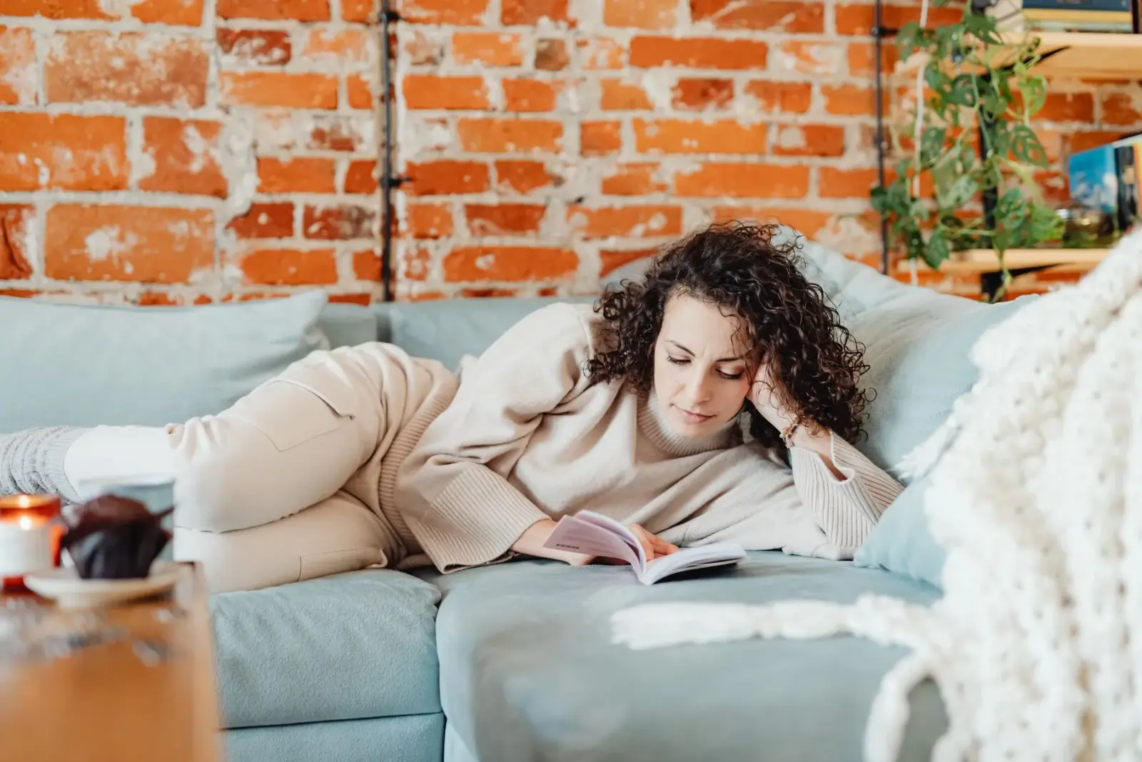 Người phụ nữ ngồi đọc sách trên ghế sofa, dáng thư giãn