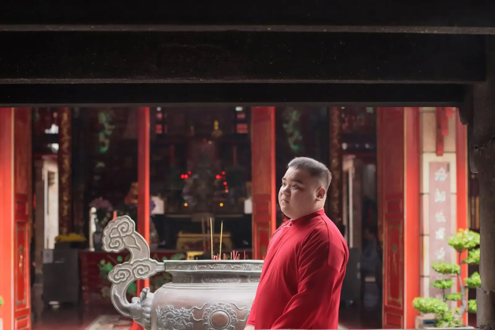 Người đàn ông mặc áo đỏ đứng bên lư hương trong ngôi chùa