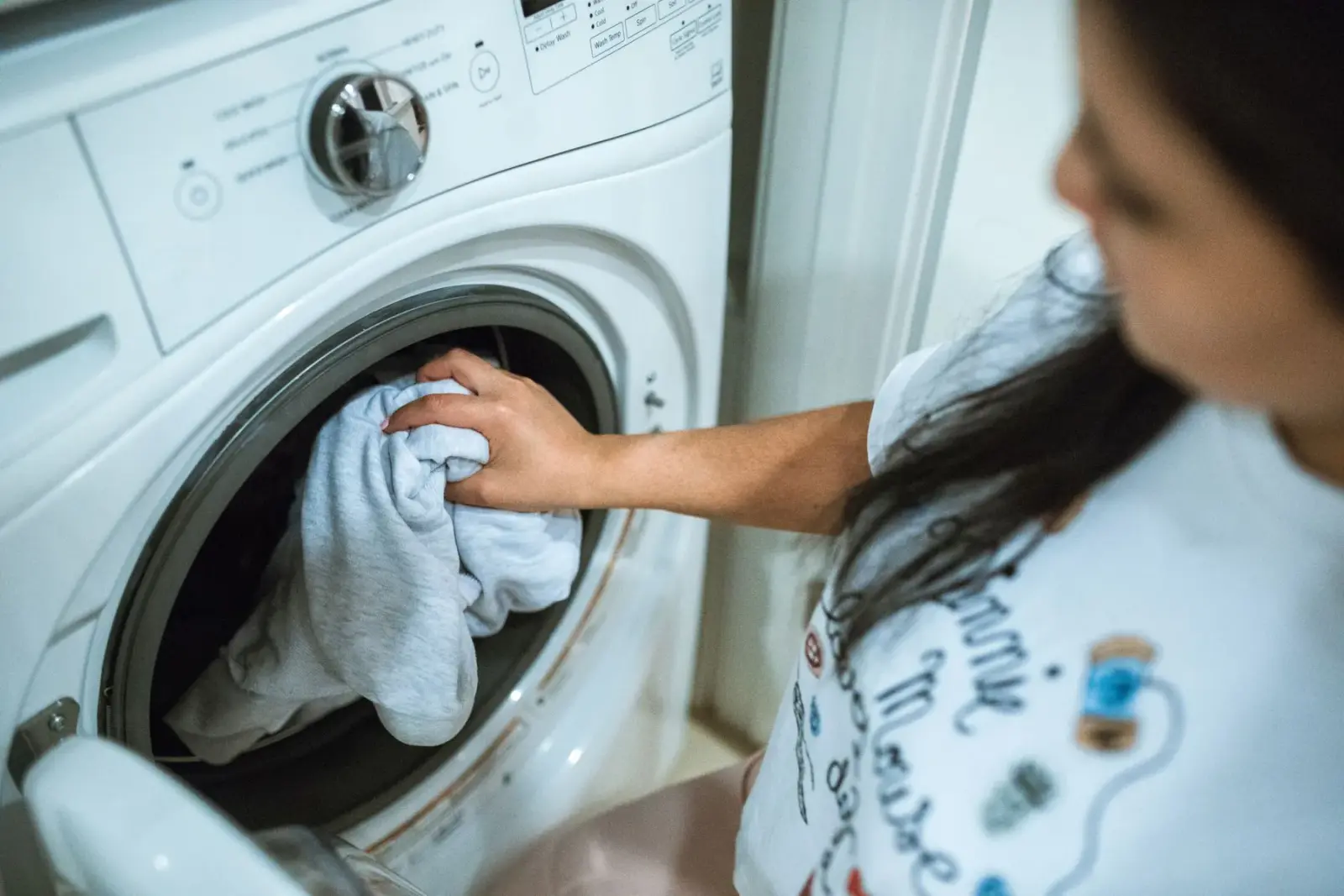 Người phụ nữ cho quần áo vào lồng máy giặt