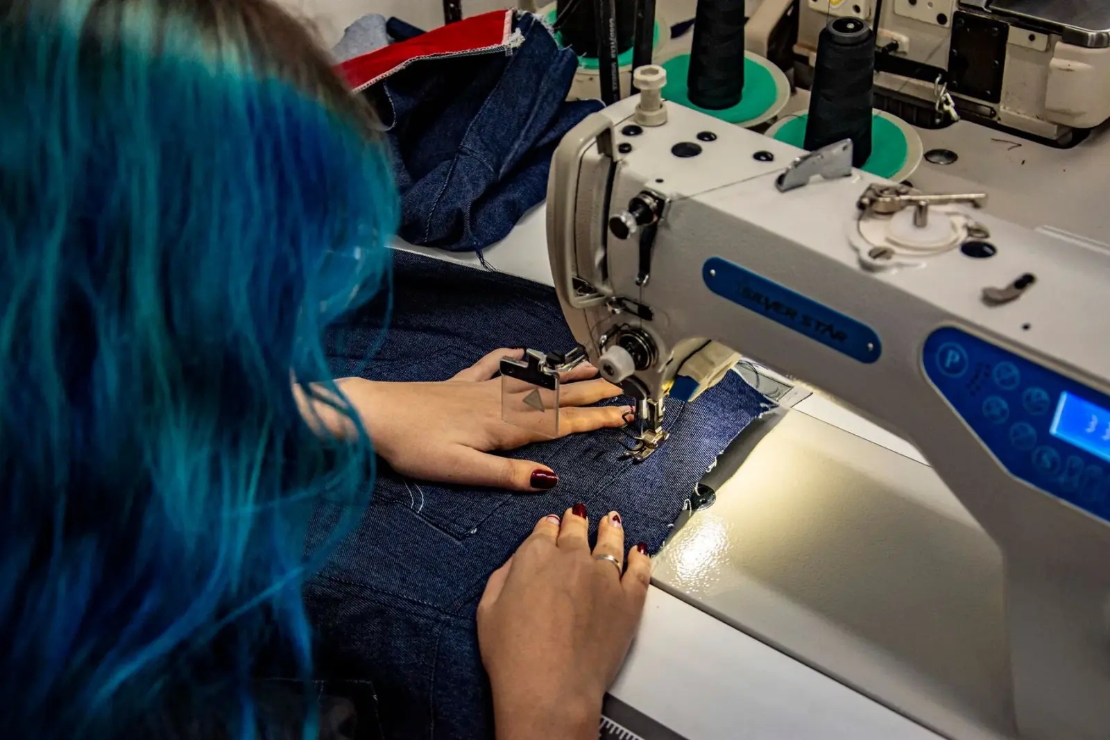 Đôi tay may vải denim trên máy may trong xưởng