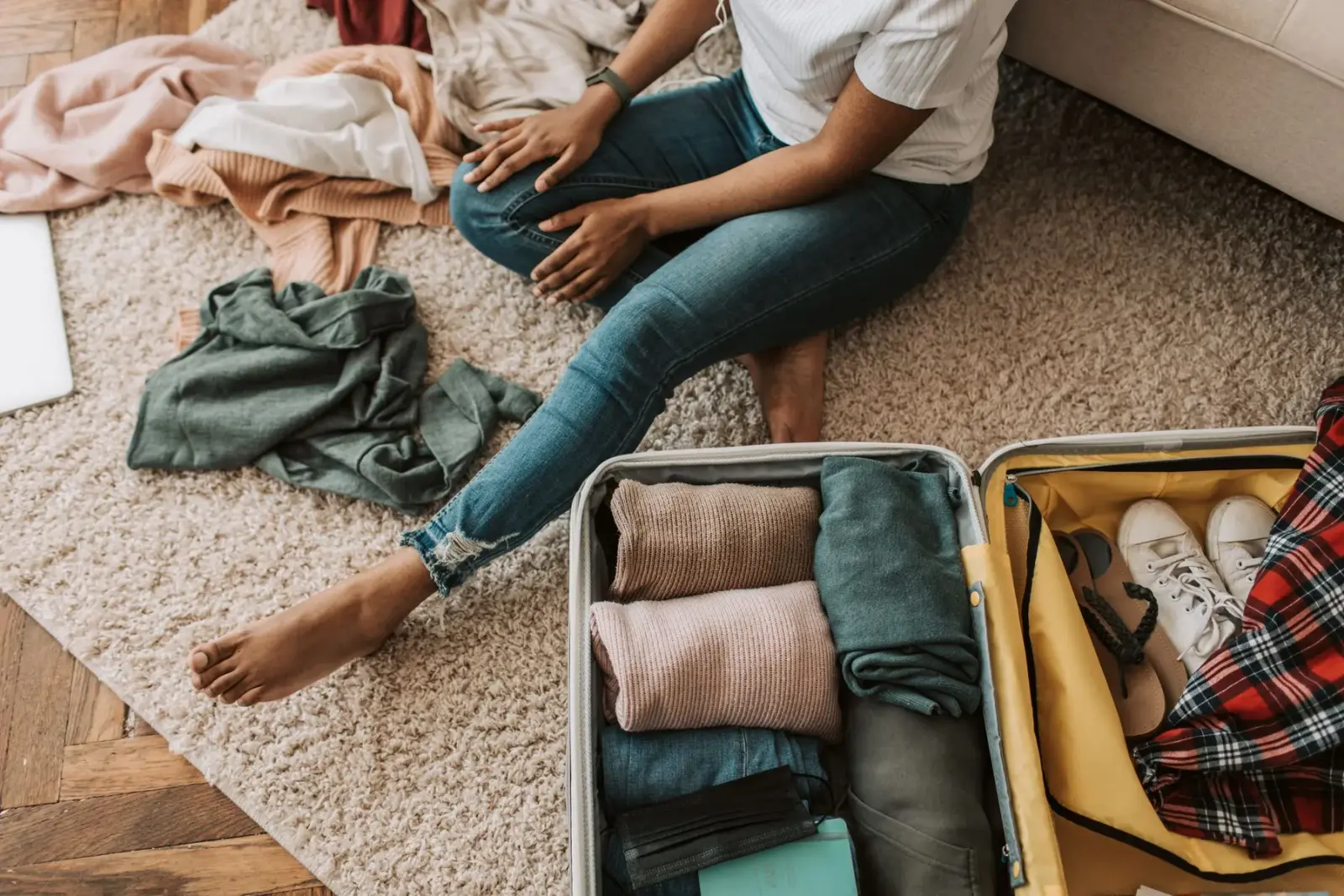 Người ngồi trên sàn xếp quần áo vào chiếc vali đang mở