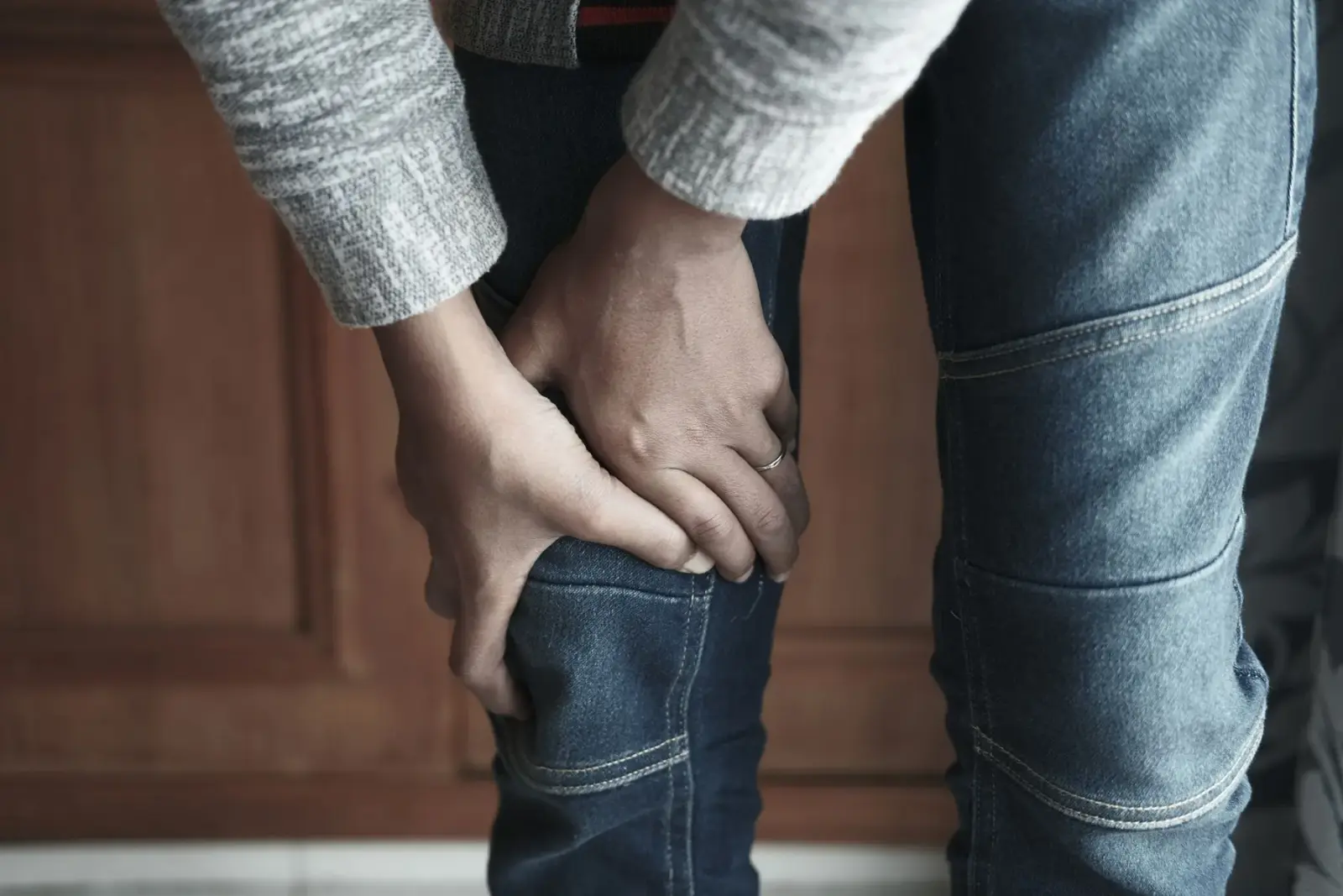 Một người giữ đầu gối trong chiếc quần jean, chụp cận