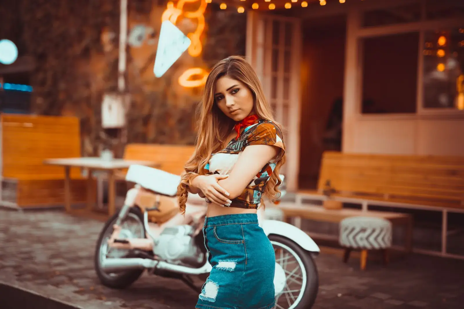 Người phụ nữ mặc chân váy denim đứng cạnh chiếc xe máy