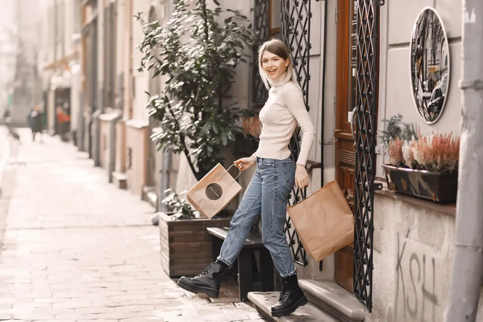 Người phụ nữ mặc quần jean ống rộng xách túi đi trên phố lát đá